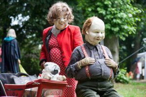 Zwei Maskenfiguren mit Hund und Kinderwagen
